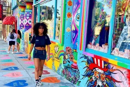 Woman walking down Haight Street with a colorful mural in the background.